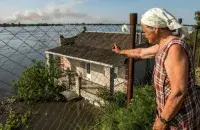Жыхарка Новай Кахоўкі на Херсоншчыне глядзіць, як вада падпальвае суседнія хаты / Reuters

